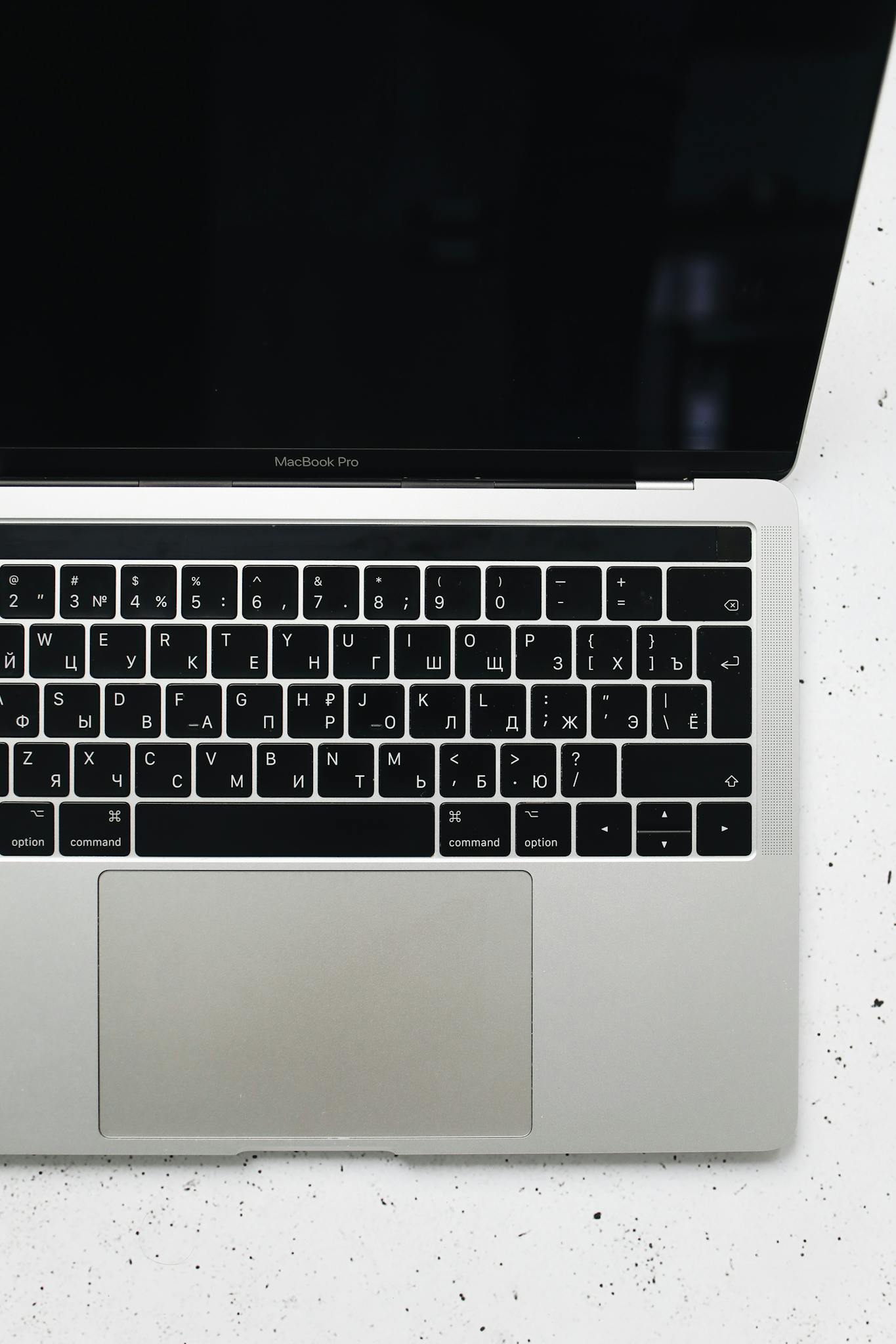 A MacBook Pro with Cyrillic keyboard on a speckled white surface, top view.